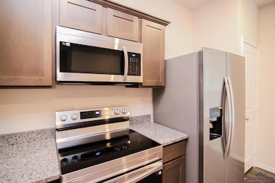Kitchen featuring appliances with stainless steel finishes, dark wood-style floors, and light stone countertops
