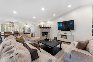 Living room with wood finished floors, recessed lighting, a stone fireplace, and lofted ceiling