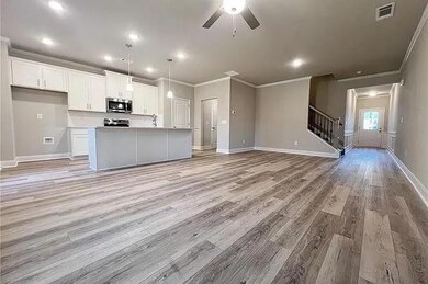 Kitchen featuring stainless steel microwave, open floor plan, ornamental molding, white cabinets, and ceiling fan