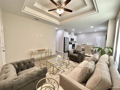 Living room featuring wood finished floors, a ceiling fan, a tray ceiling, and recessed lighting