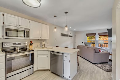 Kitchen with appliances with stainless steel finishes, a peninsula, white cabinetry, light countertops, and recessed lighting