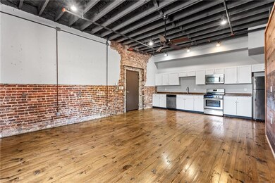 Kitchen with appliances with stainless steel finishes, brick wall, white cabinetry, a sink, and hardwood / wood-style floors