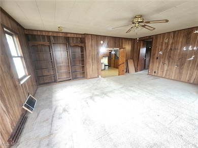 Unfurnished living room with wooden walls, light colored carpet, and a ceiling fan