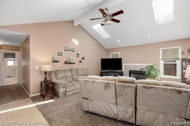 Tiled living area with a ceiling fan, beamed ceiling, carpet flooring, a fireplace, and a skylight