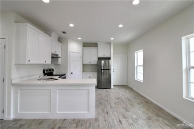 Kitchen with white cabinets, appliances with stainless steel finishes, recessed lighting, light wood-type flooring, and a peninsula