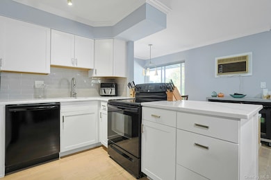Kitchen with ornamental molding, white cabinets, black appliances, decorative backsplash, and light wood-type flooring