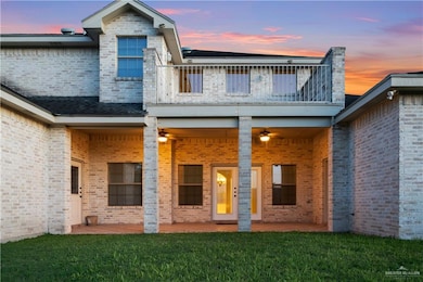 Back of house at dusk with a balcony, a yard, and brick siding