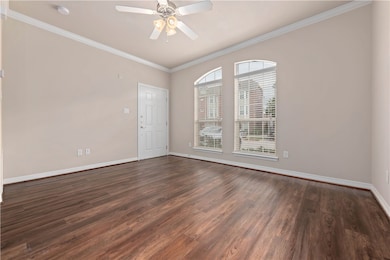 Empty room featuring ornamental molding, dark wood-style floors, and a ceiling fan