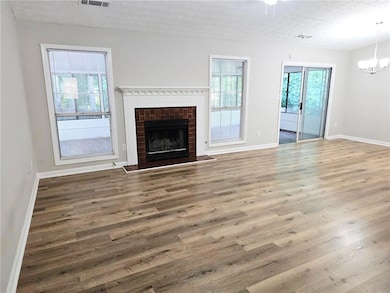 Unfurnished living room with a notable chandelier, hardwood / wood-style floors, a textured ceiling, and a fireplace
