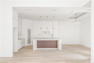 Kitchen featuring light wood finished floors, hanging light fixtures, a kitchen island, backsplash, and white cabinets