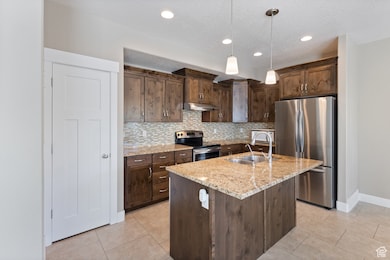 Kitchen with dark brown cabinets, stainless steel appliances, tasteful backsplash, light stone countertops, and hanging light fixtures
