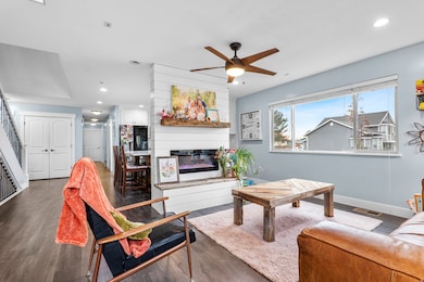 Living area with dark wood finished floors, ceiling fan, recessed lighting, a glass covered fireplace, and stairs