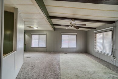 Carpeted empty room featuring ceiling fan, beam ce