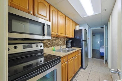 Kitchen featuring appliances with stainless steel finishes, light tile patterned flooring, brown cabinets, light countertops, and a paneled ceiling
