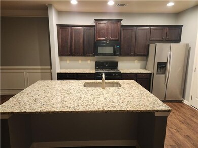 Kitchen featuring black microwave, stainless steel fridge with ice dispenser, range with gas cooktop, a sink, and an island with sink