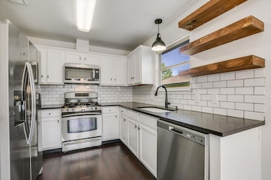 Kitchen with appliances with stainless steel finishes, white cabinets, tasteful backsplash, and dark wood-style floors