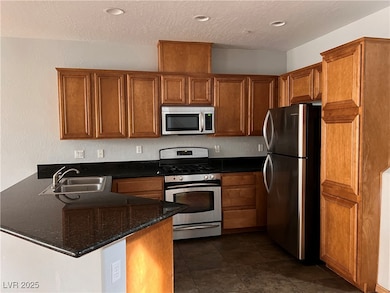 Kitchen with brown cabinetry, a peninsula, a textured ceiling, a sink, and stainless steel appliances