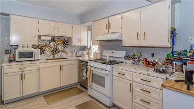 Kitchen featuring a textured wall, white appliances, cream cabinetry, light wood-style floors, and under cabinet range hood
