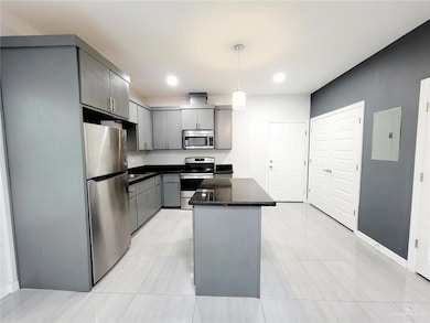 Kitchen featuring gray cabinets, appliances with stainless steel finishes, electric panel, pendant lighting, and a kitchen island