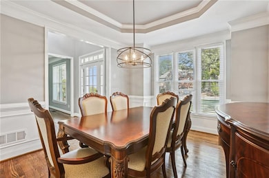 Dining room with a notable chandelier, wood finished floors, a tray ceiling, ornamental molding, and visible vents