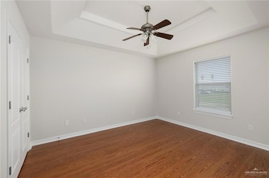 Empty room with dark hardwood / wood-style flooring, ceiling fan, and a raised ceiling
