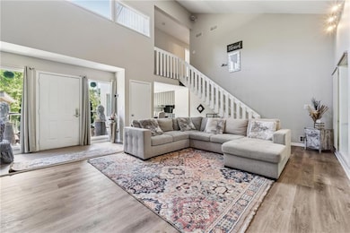 Living area featuring stairs, high vaulted ceiling, wood finished floors, and healthy amount of natural light