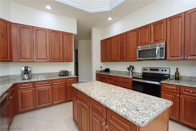 Kitchen with light tile patterned floors, crown molding, appliances with stainless steel finishes, light stone countertops, and a kitchen island