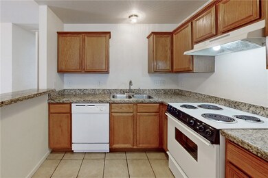 Kitchen with white appliances, brown cabinetry, under cabinet range hood, and light tile patterned floors