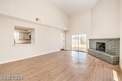 Unfurnished living room featuring high vaulted ceiling, wood finished floors, and a brick fireplace