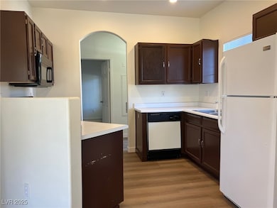 Kitchen featuring white appliances, dark brown cabinets, dark wood-type flooring, light countertops, and arched walkways