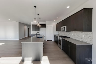 Kitchen with appliances with stainless steel finishes, decorative light fixtures, backsplash, an island with sink, and light wood-style floors