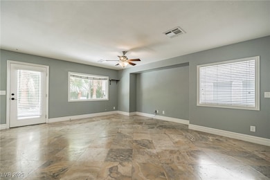 Empty room featuring plenty of natural light, ceiling fan, and light stone finish flooring