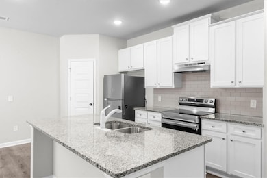Kitchen with appliances with stainless steel finishes, under cabinet range hood, a sink, an island with sink, and white cabinets