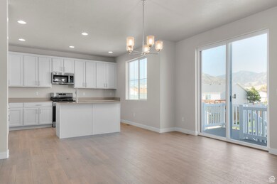 Kitchen featuring pendant lighting, white cabinetry, light countertops, stainless steel appliances, and a kitchen island