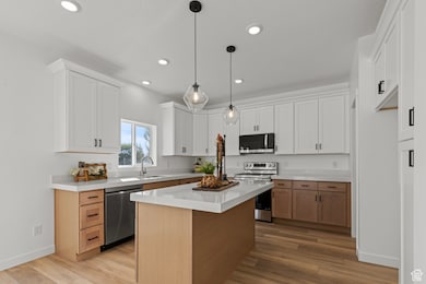 Kitchen featuring stainless steel appliances, light wood finished floors, a kitchen island, white cabinetry, and recessed lighting.