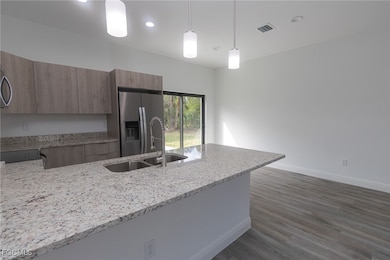 Kitchen with light stone counters, stainless steel refrigerator with ice dispenser, a sink, and modern cabinets