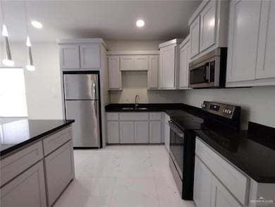 Kitchen with appliances with stainless steel finishes, light marble finish floors, dark countertops, and recessed lighting