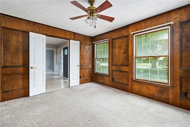 Unfurnished bedroom featuring carpet flooring, wooden walls, multiple windows, a textured ceiling, and a ceiling fan