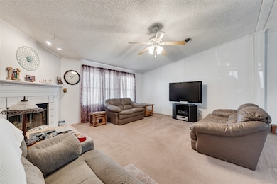 Living area featuring light colored carpet, vaulted ceiling, a textured ceiling, a tiled fireplace, and a ceiling fan