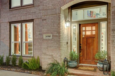 Warm brick detail frames the custom wood front door with glass inset, accented by new hardware and fresh landscaping. Step inside to soaring ceilings and natural light. The entry sets a refined tone for the home’s recent updates throughout.