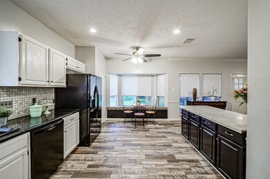 An alternate view of the kitchen highlights the fine finishes that include black granite countertops with white cabinetry, married to the black cabinetry and white quartz counters on the peninsula by a beautiful black and white basketweave pattern tile backsplash.
