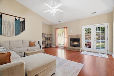 Living area with wood finished floors, a fireplace, a ceiling fan, french doors, and high vaulted ceiling