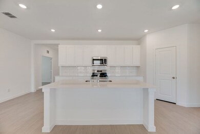 Kitchen with appliances with stainless steel finishes, backsplash, light countertops, light wood-style floors, and white cabinets
