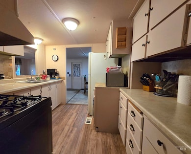 Kitchen featuring white cabinets, light wood-style flooring, light countertops, black gas stove, and tasteful backsplash