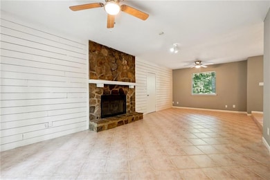 Unfurnished living room featuring a stone fireplace, light tile patterned floors, and ceiling fan