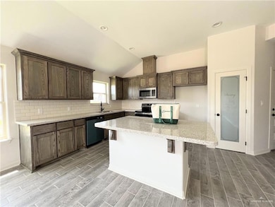 Kitchen with light wood-type flooring, decorative backsplash, appliances with stainless steel finishes, a kitchen island, and lofted ceiling