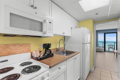 Kitchen with white appliances, a sink, light tile patterned flooring, white cabinetry, and a paneled ceiling
