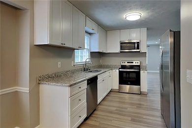 Kitchen featuring stainless steel appliances, light wood finished floors, light stone countertops, white cabinetry, and a textured ceiling