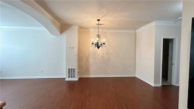 Unfurnished dining area with ornamental molding, dark wood-style floors, arched walkways, a chandelier, and baseboards
