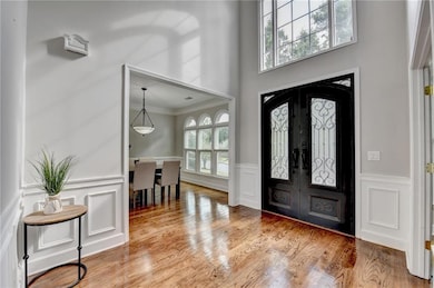 Foyer entrance with wood finished floors, french doors, a decorative wall, a towering ceiling, and ornamental molding